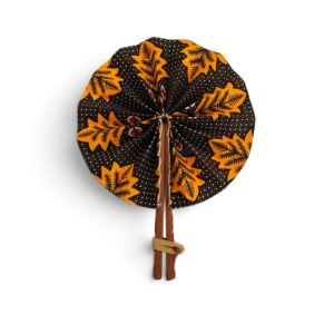 Éventail rond en tissu wax orange et noir à motifs de feuilles, doté de manches en simili cuir marron.